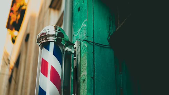 Classic barber shop sign with red, white and blue stripes on green wall