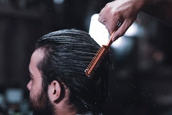 Hairdresser combing client's hair with orange comb in salon