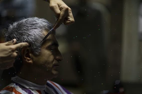 Hairdresser cutting client's grey hair with scissors in salon